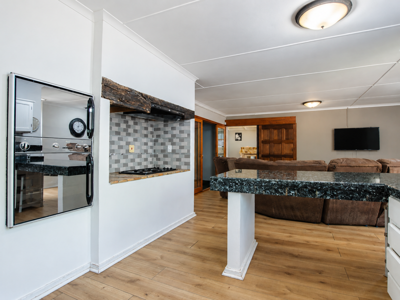 Open-plan kitchen and living area featuring granite countertops, built-in oven, gas hob, and laminate flooring with a rustic timber beam accent.