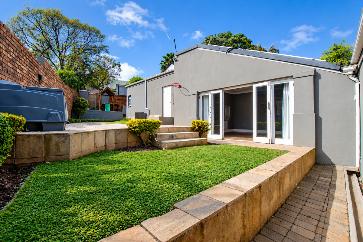 Rear exterior view featuring a paved patio, grass lawn, stone retaining walls, and french doors leading into the home.