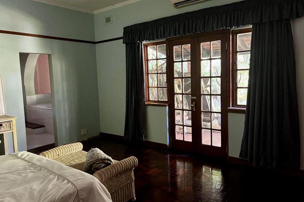 Spacious bedroom featuring polished timber flooring, air conditioning unit, and French doors providing direct access to the outdoor area.