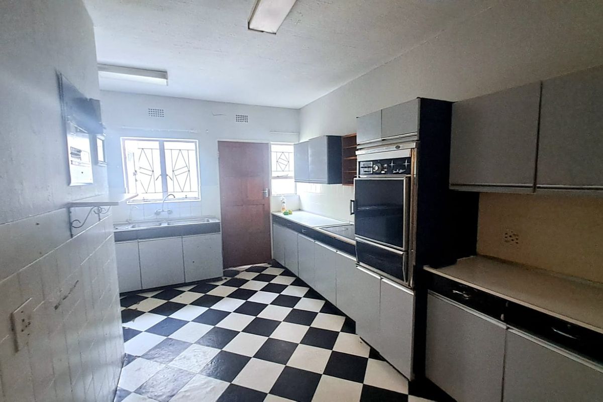 A dated kitchen featuring original cabinetry, built-in oven, double sink, and a distinctive black and white checkered floor.