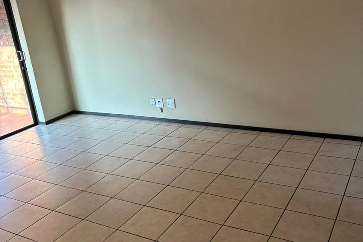 An empty living room featuring neutral wall paint, tiled flooring, and a sliding glass door providing access to an outdoor area.