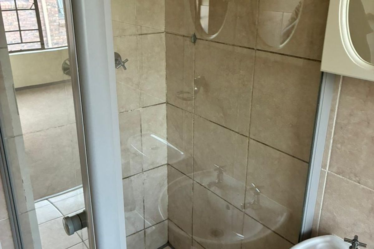 A functional bathroom featuring a glass-enclosed shower with tiled walls and a pedestal basin, showing standard wear and dated finishes.