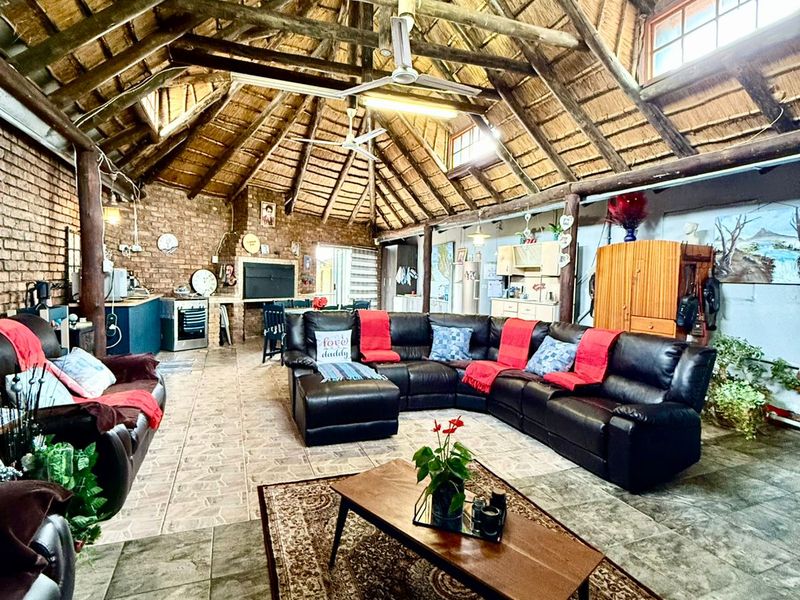 Spacious open-plan living area featuring a high vaulted thatched ceiling with exposed timber trusses, brick walls, and tiled flooring.