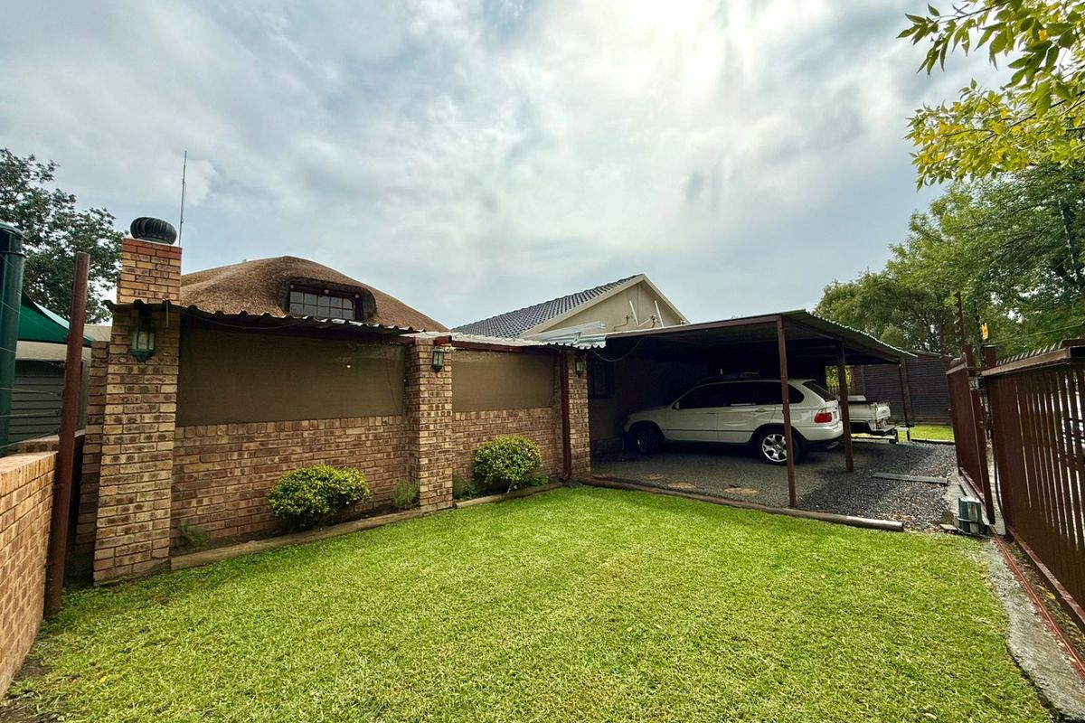 Rear exterior view featuring a lawn, brick wall, and a covered carport area with gravel driveway.