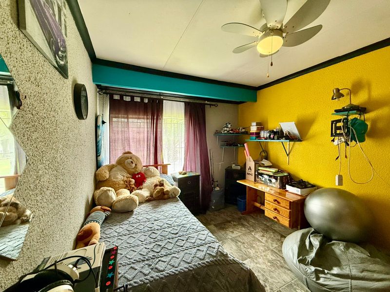 A bedroom featuring tiled flooring, a ceiling fan, and built-in shelving, currently utilized as a functional living space.