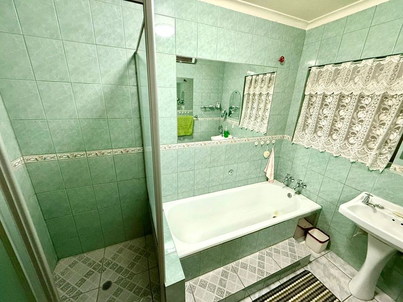 A dated bathroom featuring a built-in bathtub, separate shower enclosure, and a pedestal sink, finished with full-height green ceramic wall tiles.