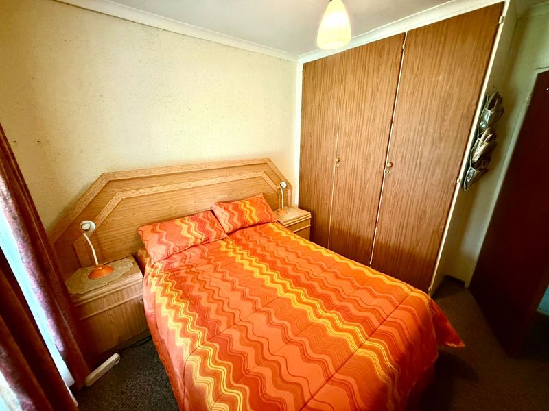 A bedroom featuring built-in wooden wardrobes, carpeted flooring, and coving, presenting a dated aesthetic suitable for modernization.