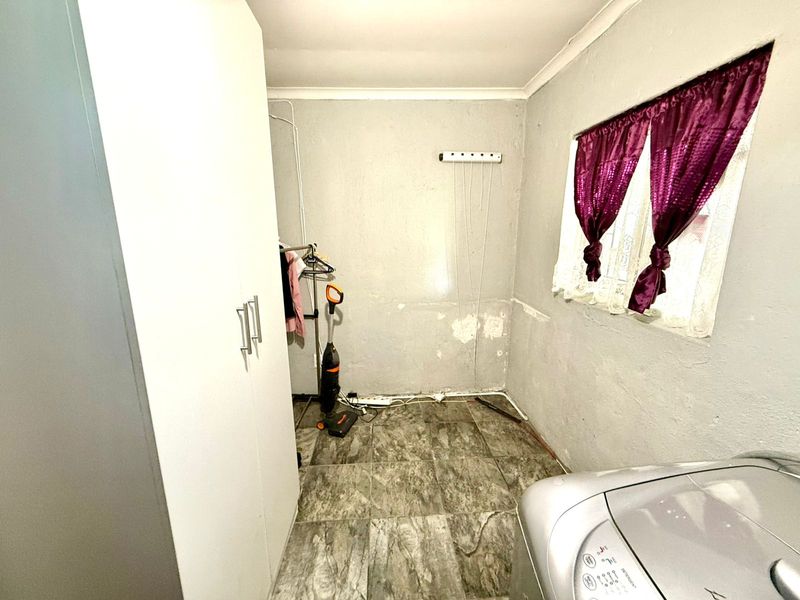 A functional laundry room featuring tiled flooring, a wall-mounted drying rack, and built-in storage cabinetry.