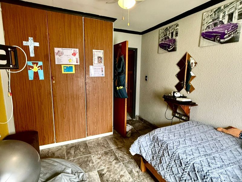 A bedroom featuring tiled flooring, a ceiling fan, and built-in wooden cupboards.