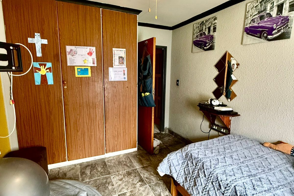 A bedroom featuring tiled flooring, a ceiling fan, and built-in wooden cupboards.