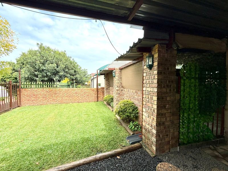 A covered patio area featuring brick pillars and a corrugated roof, overlooking a private garden with a brick boundary wall.