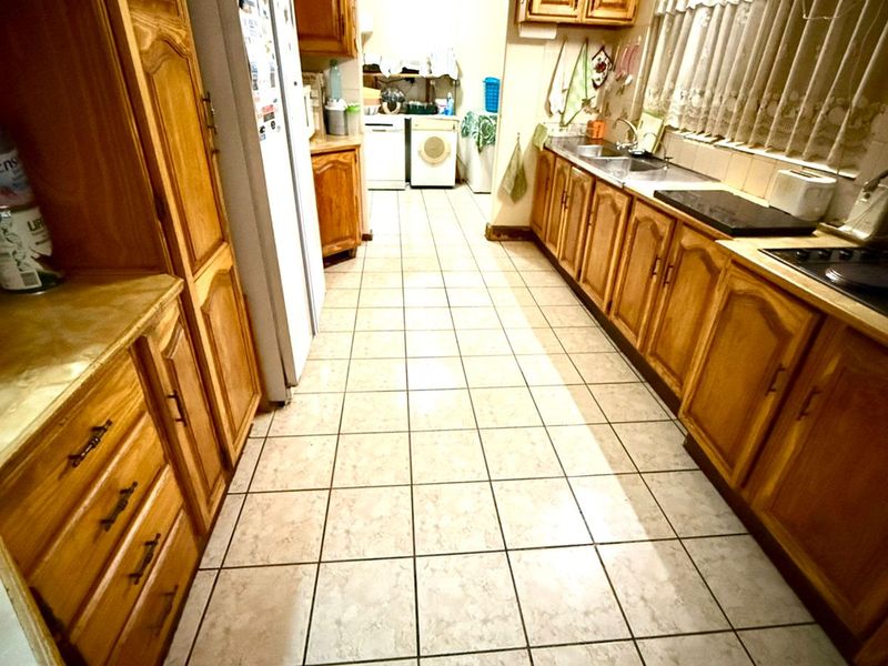 A functional kitchen featuring timber cabinetry, tiled flooring, and a double bowl sink, with an adjacent laundry area visible in the background.