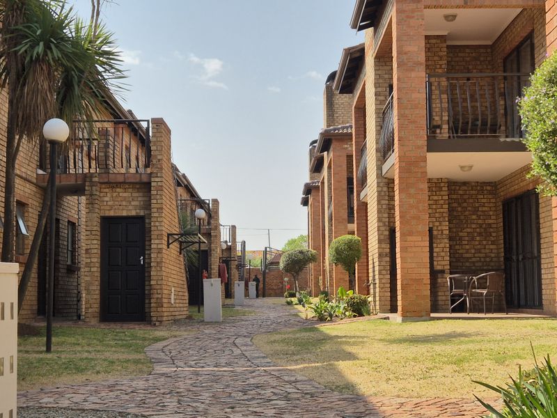 A view of the townhouse complex exterior featuring face brick facades, paved walkways, and private balconies overlooking a landscaped garden area.