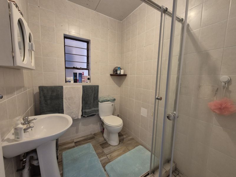 A functional bathroom featuring a pedestal basin, toilet, and a glass-enclosed shower with neutral wall tiling and wood-look floor tiles.