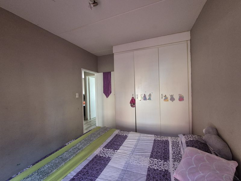 A bedroom featuring a built-in wardrobe with white doors, neutral wall tones, and access to an adjacent hallway.
