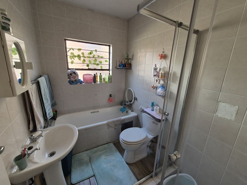 A functional bathroom featuring a bathtub, separate shower enclosure, pedestal basin, and toilet, with tiled walls and a window with security bars.
