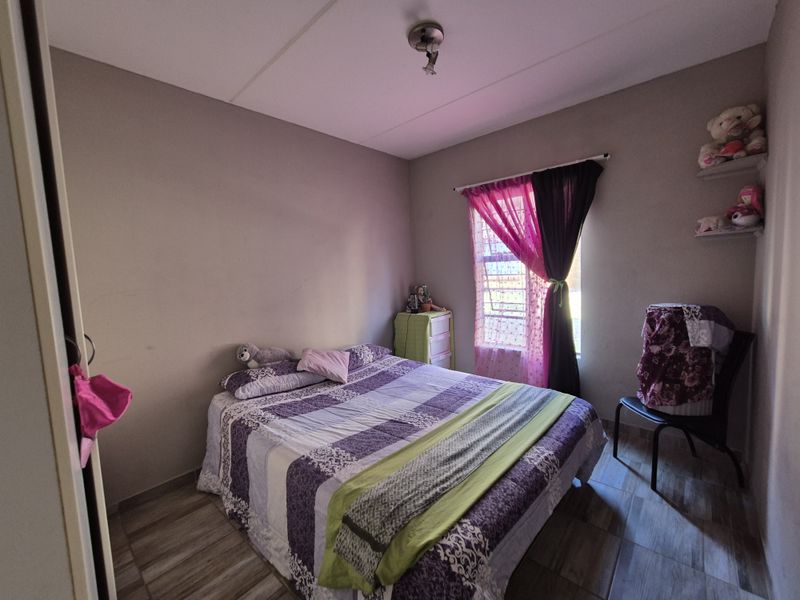 A functional bedroom featuring tiled flooring, a window with security bars, and built-in wall shelving.