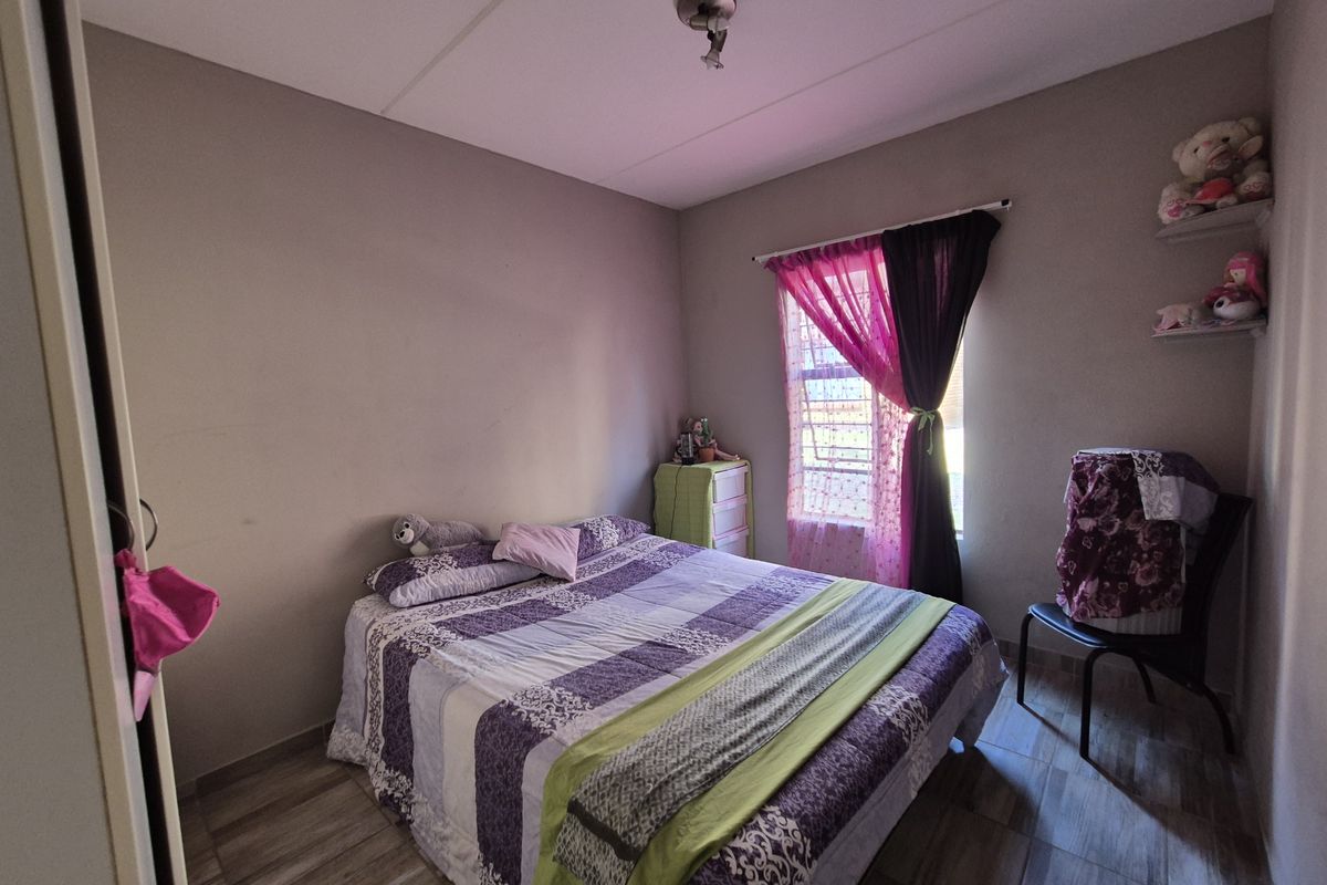 A functional bedroom featuring tiled flooring, a window with security bars, and built-in wall shelving.