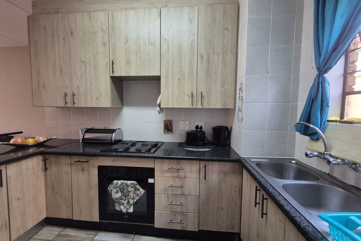 A functional kitchen featuring light wood-look cabinetry, dark granite countertops, a built-in oven with electric hob, and a double stainless steel sink.