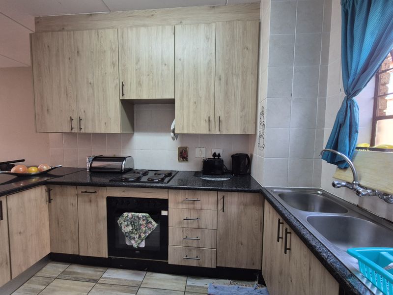 A functional kitchen featuring light wood-look cabinetry, dark granite countertops, a built-in oven with electric hob, and a double stainless steel sink.