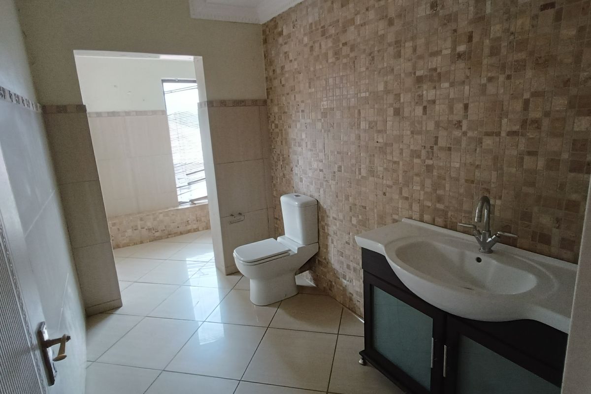 A bathroom featuring a vanity with a basin, a toilet, and mosaic wall tiling, with an adjacent tiled area visible through the doorway.