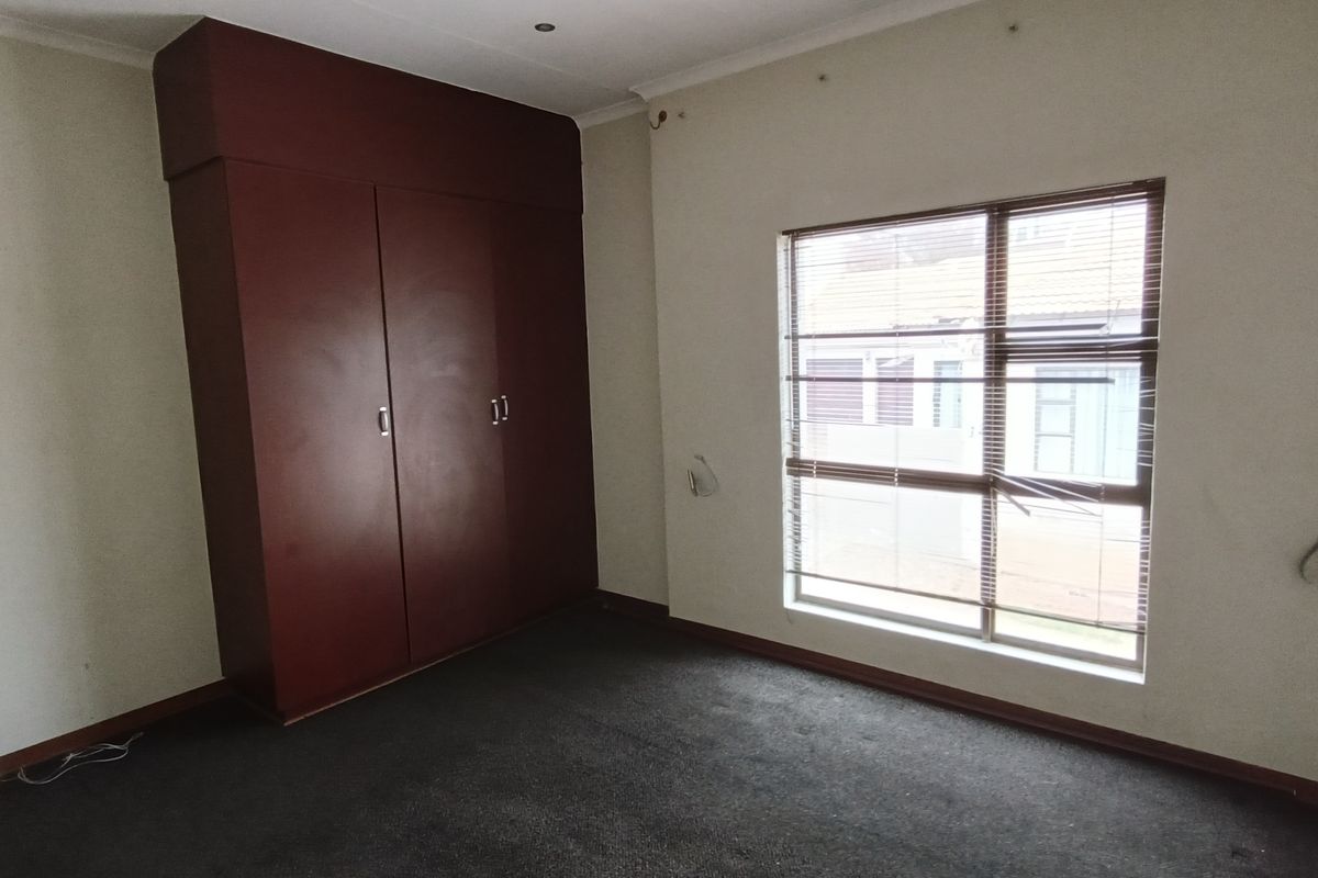 A bedroom featuring built-in dark wood cabinetry, carpeted flooring, and a large window with fitted blinds.