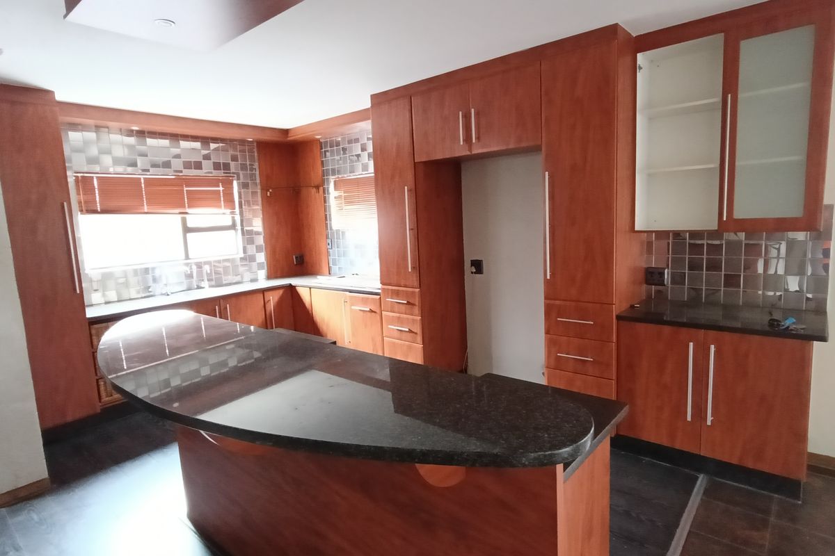 A spacious kitchen featuring cherry-wood cabinetry, dark granite countertops, a central breakfast island, and a tiled backsplash.