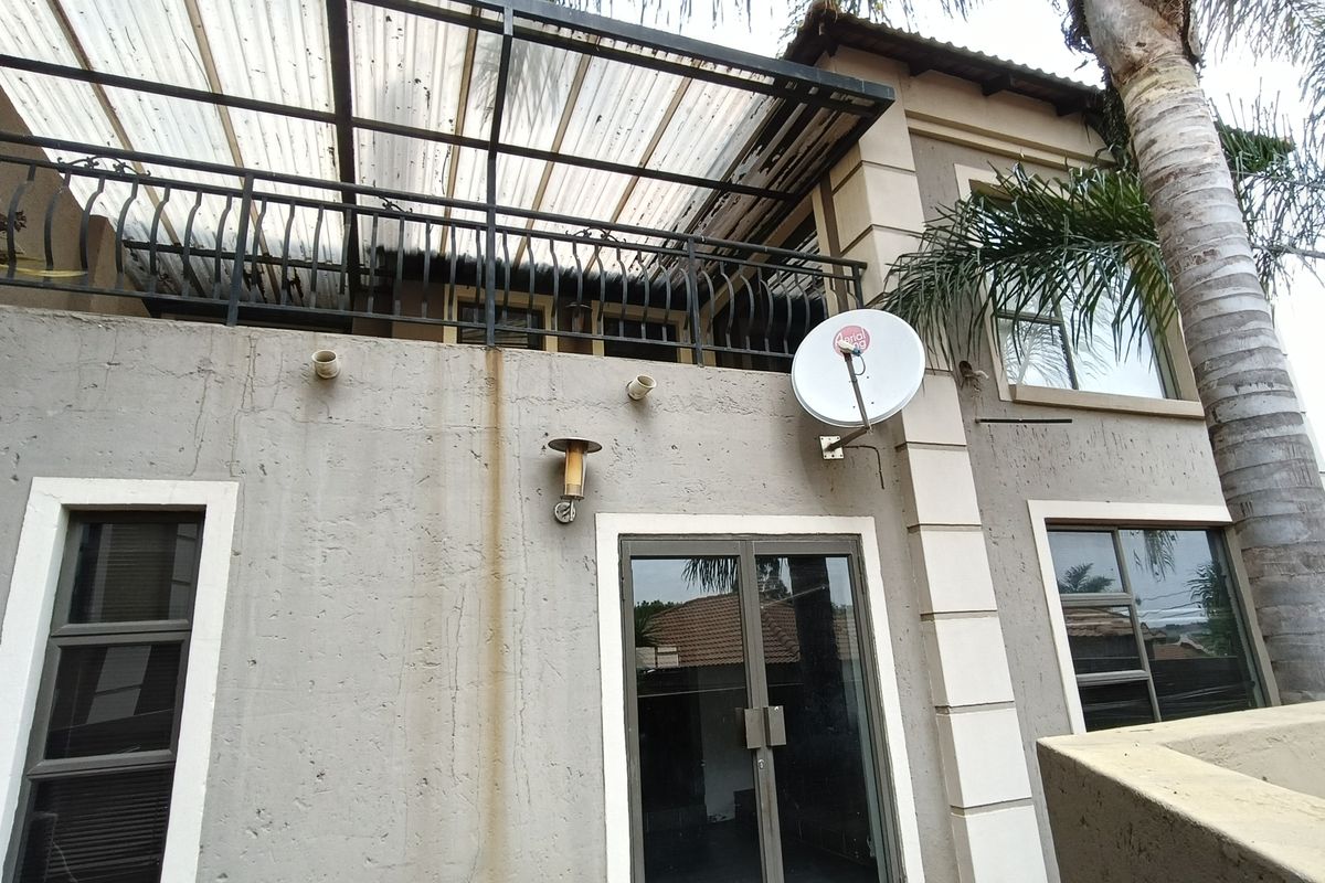 Rear exterior view of the townhouse featuring a covered patio area with metal railing and integrated wall lighting.