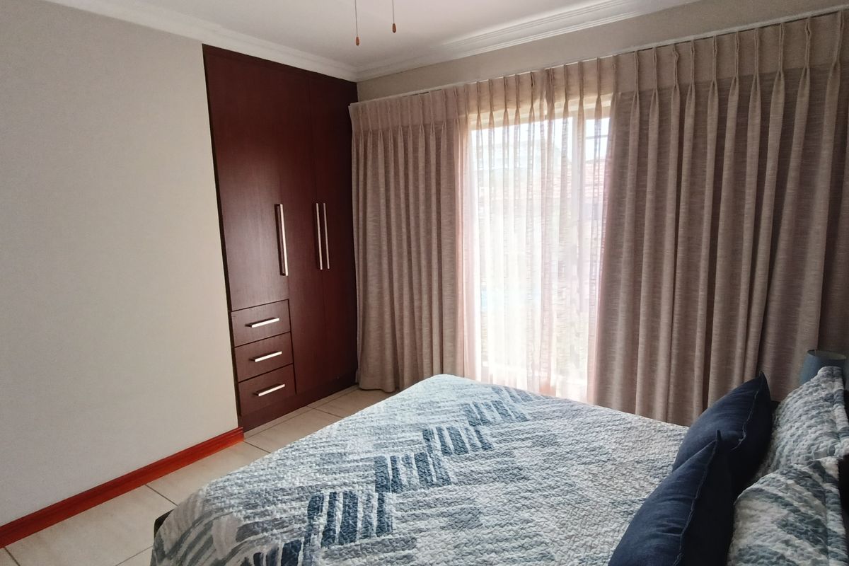 A well-maintained bedroom featuring built-in dark wood cabinetry and large sliding glass doors with floor-to-ceiling curtains providing natural light.