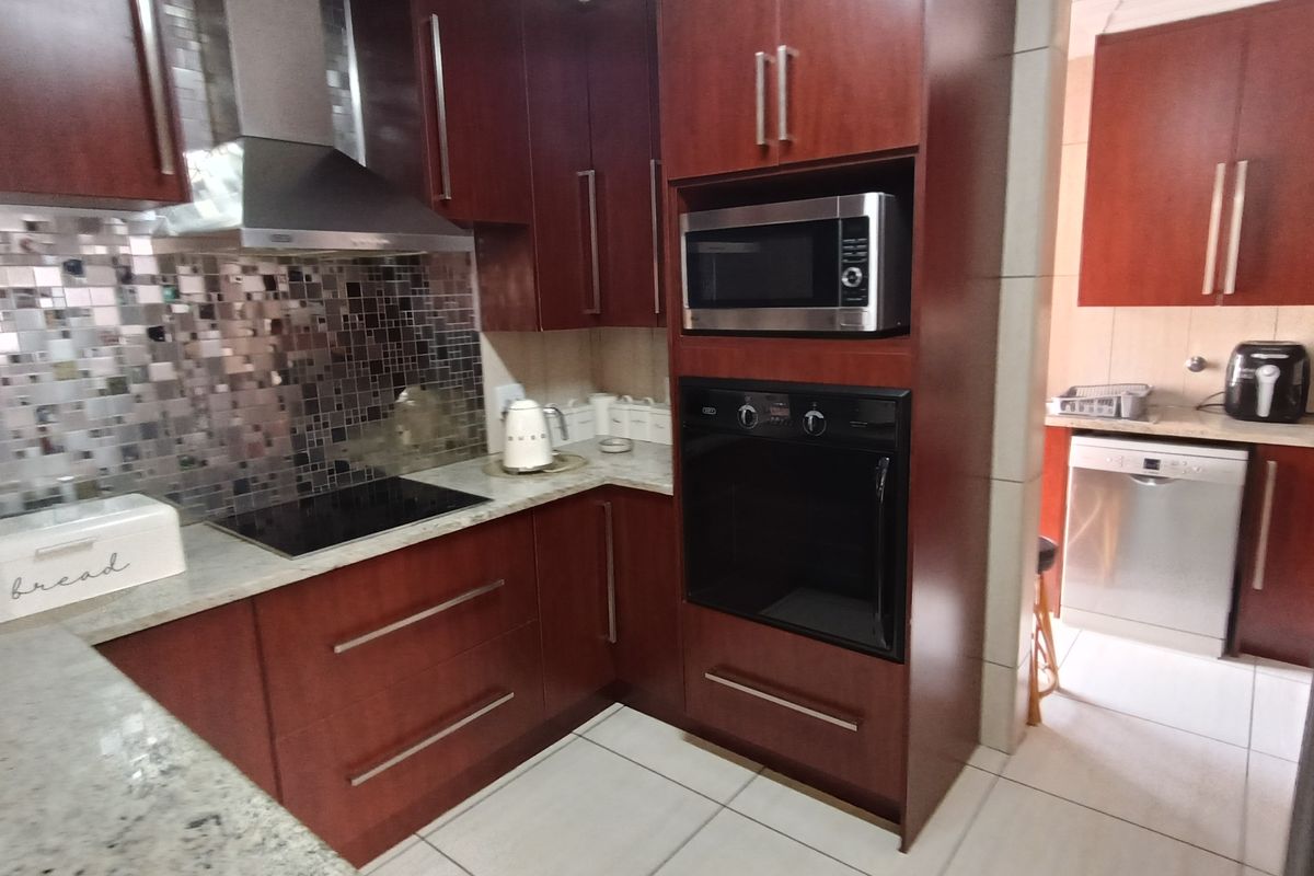 A functional kitchen featuring dark wood cabinetry, granite countertops, a mosaic tile backsplash, built-in oven, microwave, and stainless steel extractor fan.