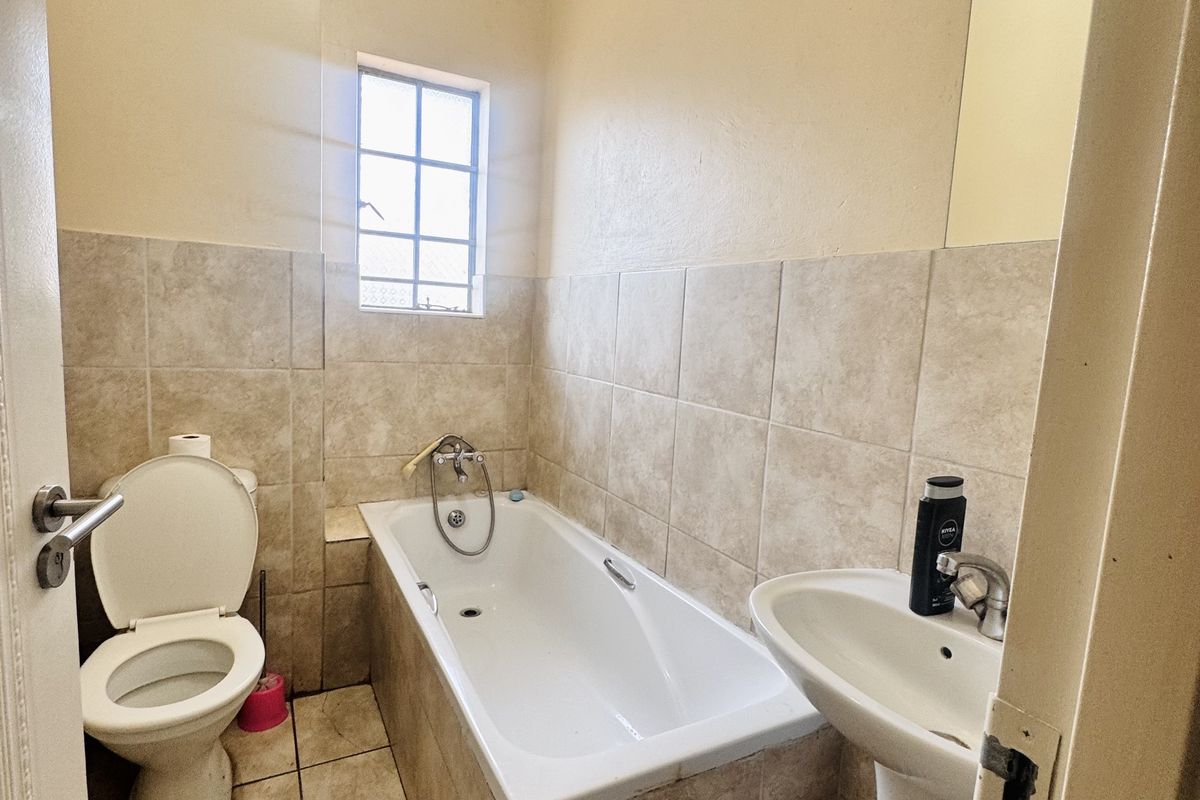 A functional bathroom featuring a bathtub, pedestal basin, and toilet with neutral wall tiling and tiled flooring.