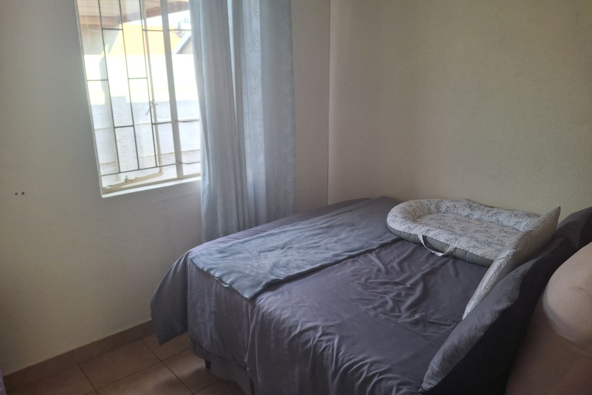 A functional bedroom featuring tiled flooring and a window with security bars, providing natural light and ventilation.