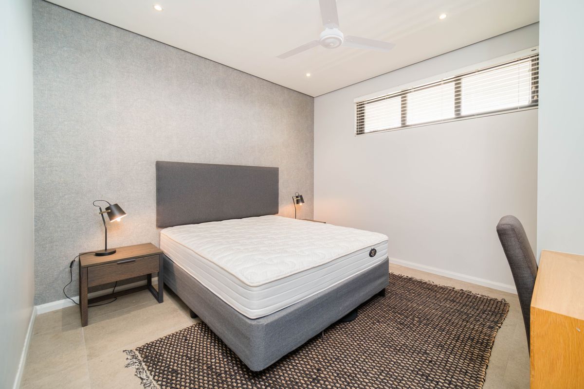 A modern bedroom featuring a textured feature wall, recessed ceiling lighting, a ceiling fan, and horizontal window blinds.