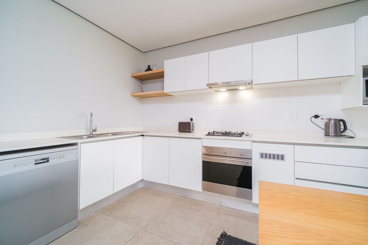 Modern kitchen featuring white cabinetry, stone countertops, integrated stainless steel oven, gas hob, extractor fan, and tiled flooring.