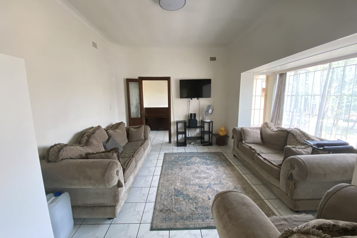 A living room featuring tiled flooring, a large bay window, and a central ceiling light fixture.