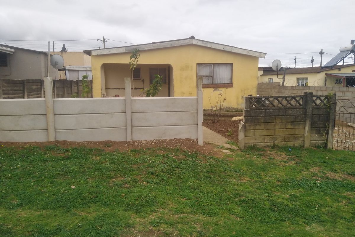 Rear view of a detached house featuring a covered patio, concrete boundary walls, and a small garden area requiring maintenance.