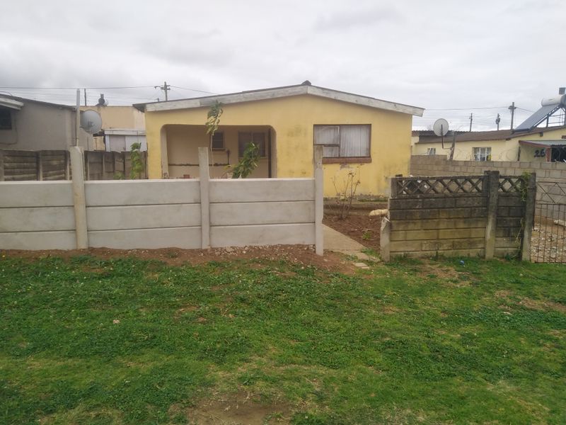 Rear view of a detached house featuring a covered patio, concrete boundary walls, and a small garden area requiring maintenance.