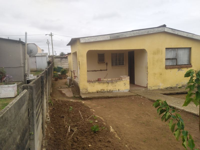 Front view of a single-story house featuring a covered patio, concrete walkway, and precast boundary wall, showing signs of significant exterior wear.