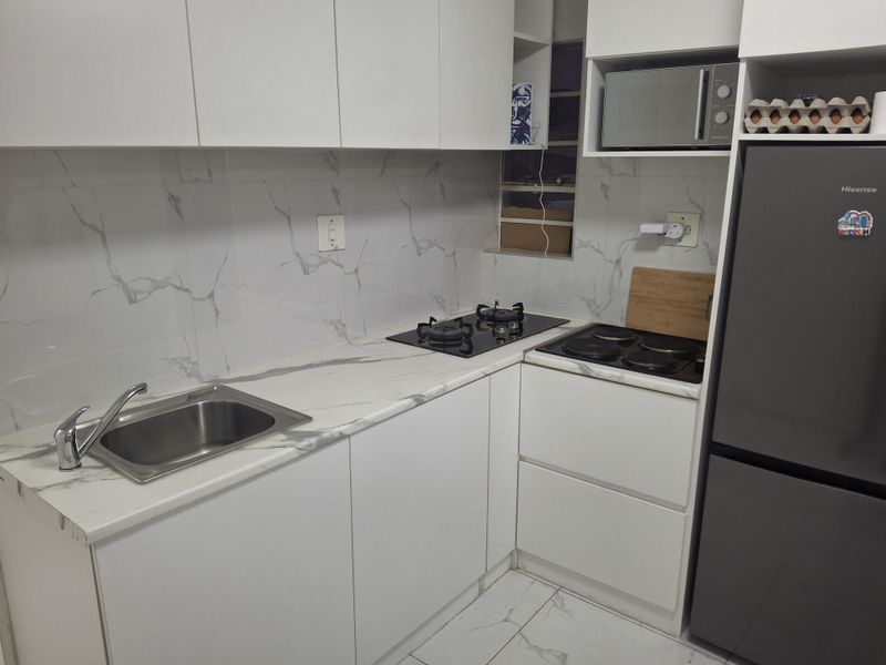 Modern kitchen featuring white cabinetry, marble-look countertops and wall tiles, dual hobs, and a built-in microwave.