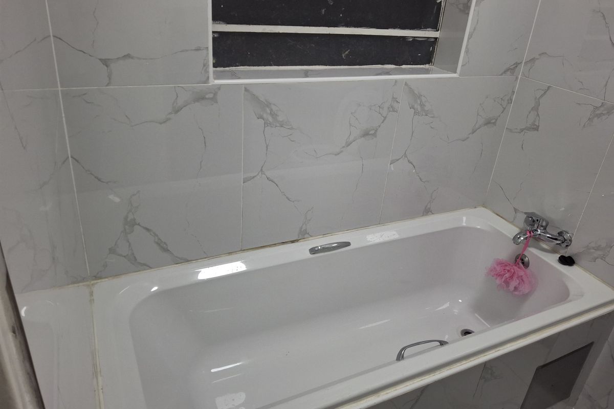 A clean bathroom featuring a built-in bathtub with marble-look wall tiling and a louver window for ventilation.