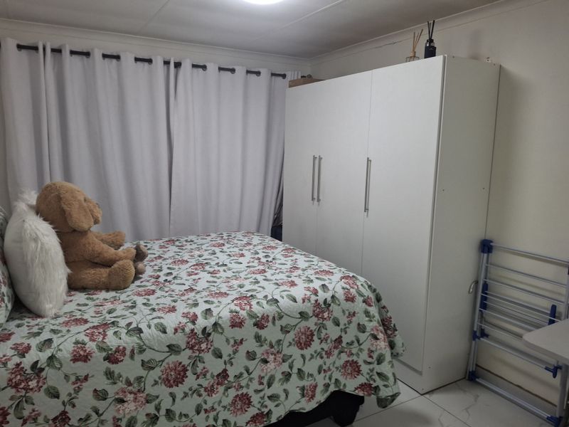 A functional bedroom featuring tiled flooring, a built-in wardrobe, and neutral wall finishes, providing a clean and practical living space.