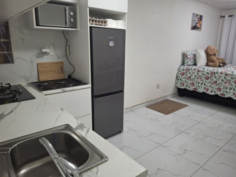 Compact open-plan studio apartment featuring a modern kitchenette with marble-effect countertops, electric hob, and tiled flooring throughout.