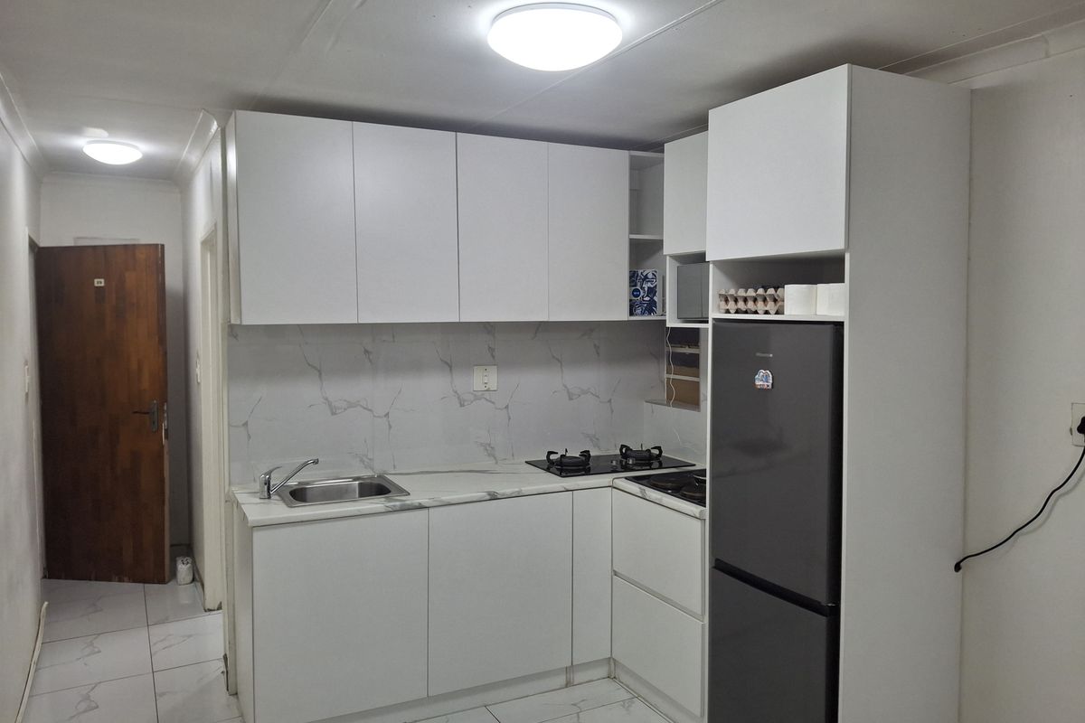 A compact, modern kitchen featuring white cabinetry, marble-effect countertops, a gas hob, and tiled finishes throughout.