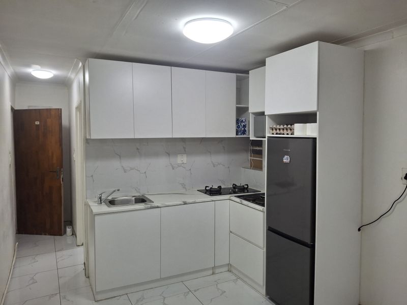 A compact, modern kitchen featuring white cabinetry, marble-effect countertops, a gas hob, and tiled finishes throughout.
