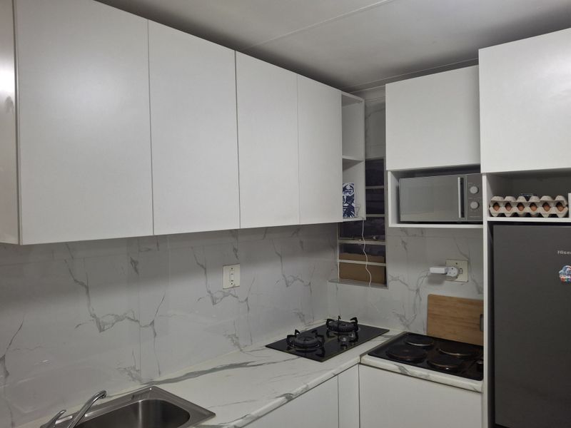 Modern kitchen featuring white cabinetry, marble-look countertops and backsplash, dual hob setup, and integrated microwave.