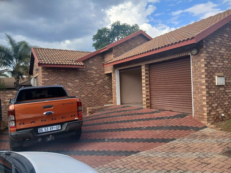Front view of a face brick house featuring a double garage with roller shutter doors and a paved driveway.