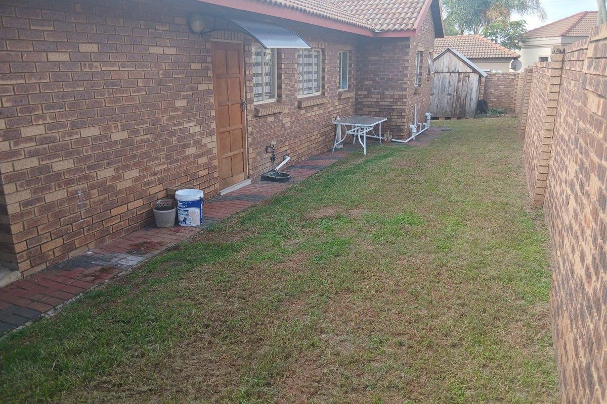 A view of the rear exterior of the house featuring face brick walls, a tiled roof, and a paved walkway alongside a lawn area.