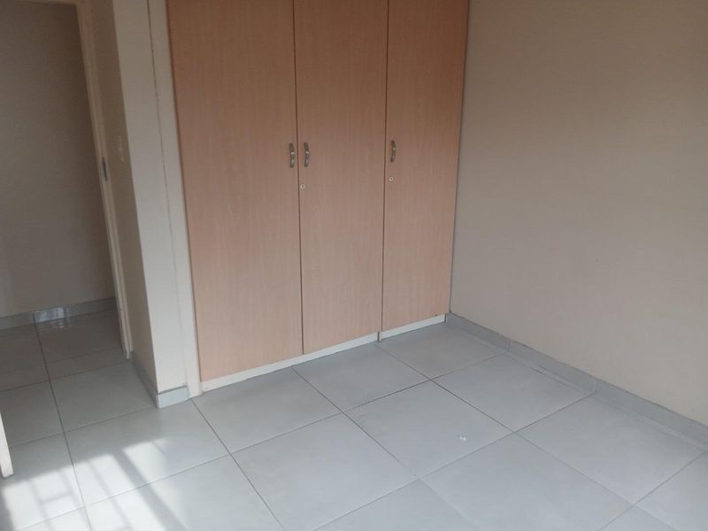 An empty bedroom featuring light wood-finish built-in cupboards and neutral tiled flooring.