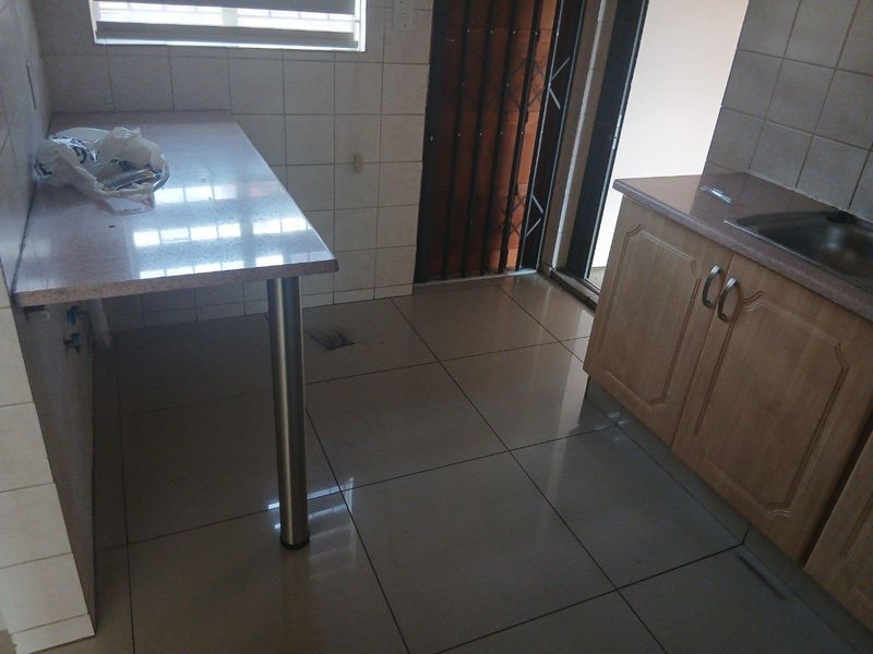 A functional kitchen area featuring tiled flooring, built-in cabinetry with stone countertops, a stainless steel sink, and a security gate at the entrance.