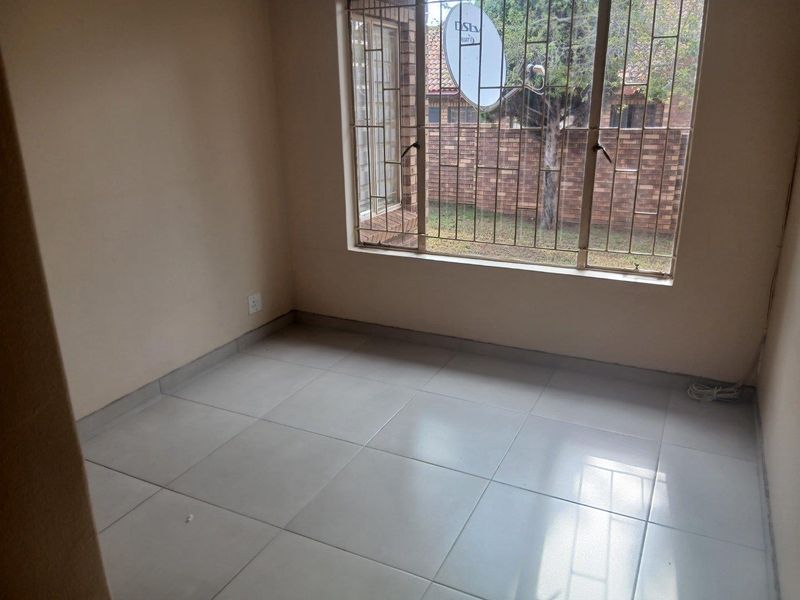 A vacant bedroom featuring neutral tiled flooring and a large window fitted with security bars, offering a clean and blank canvas.